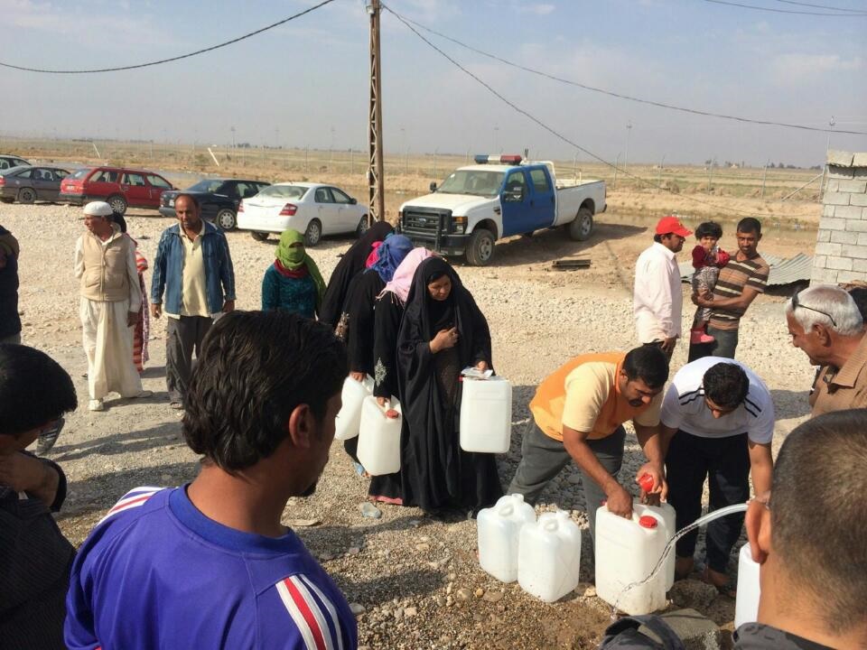 Iraqi civilians line up to get fresh water from Rainfresh's water treatment system